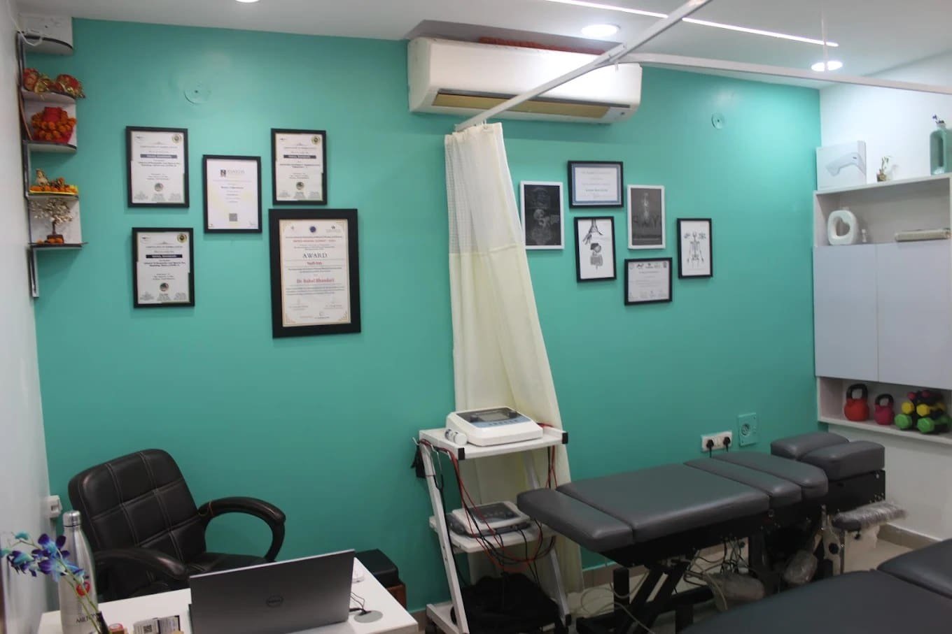 A clean, well-lit physiotherapy treatment room with certificates and awards on the wall at Symphysio, Sarita Vihar